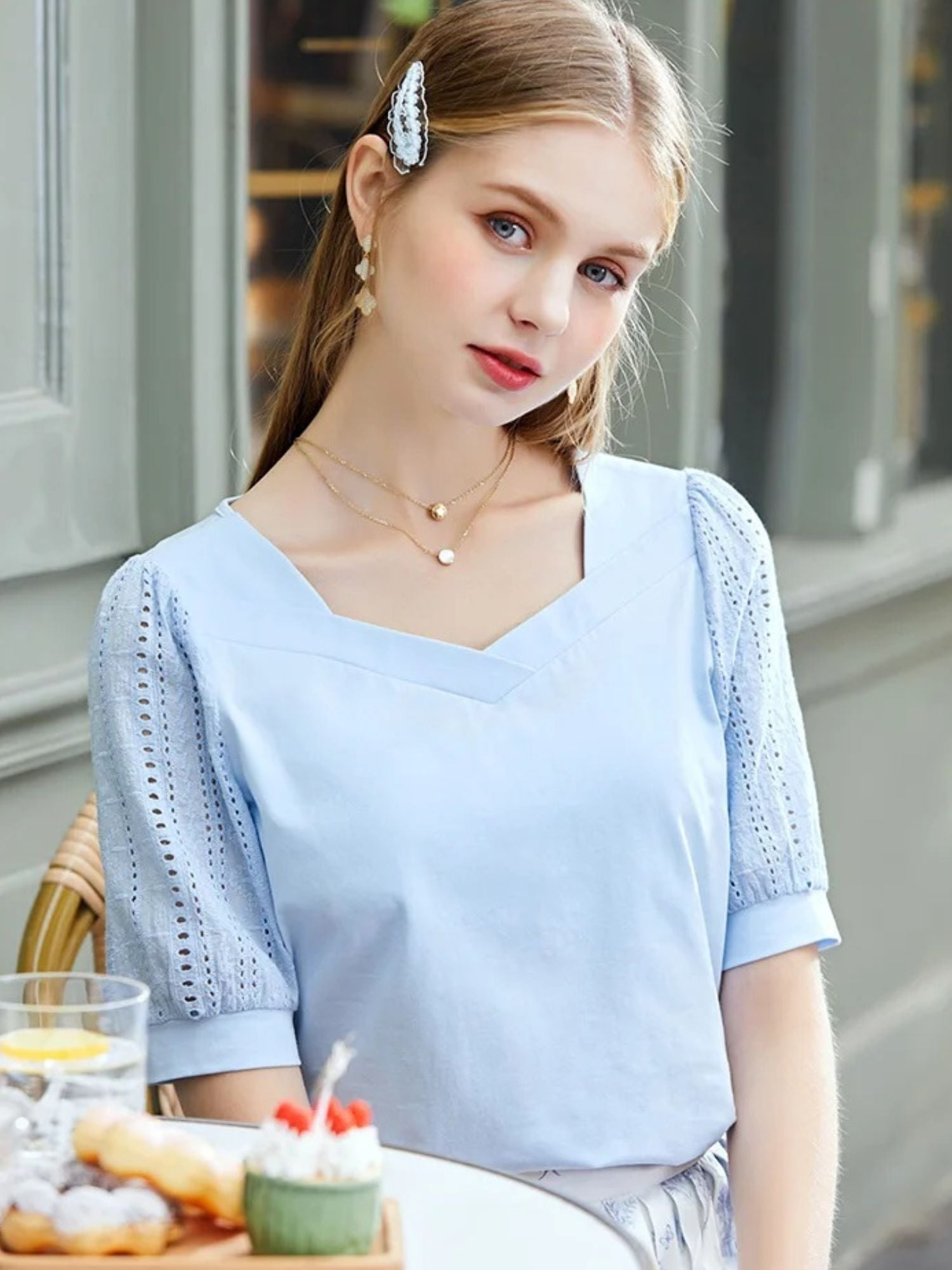 Woman in light blue V-neck blouse with lace sleeves sitting at a café table.