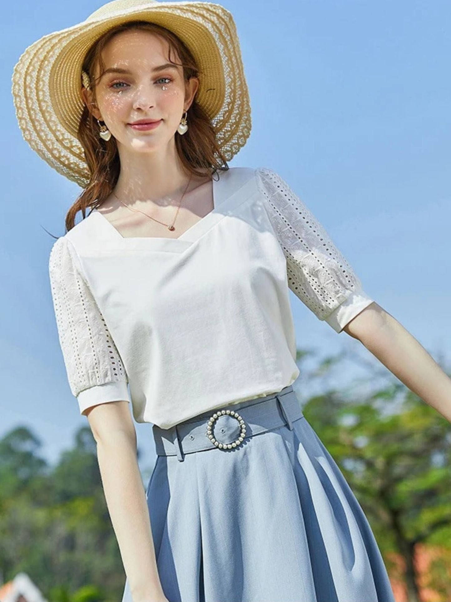 Woman in white blouse with mesh sleeves and belt, looking up in the sun.