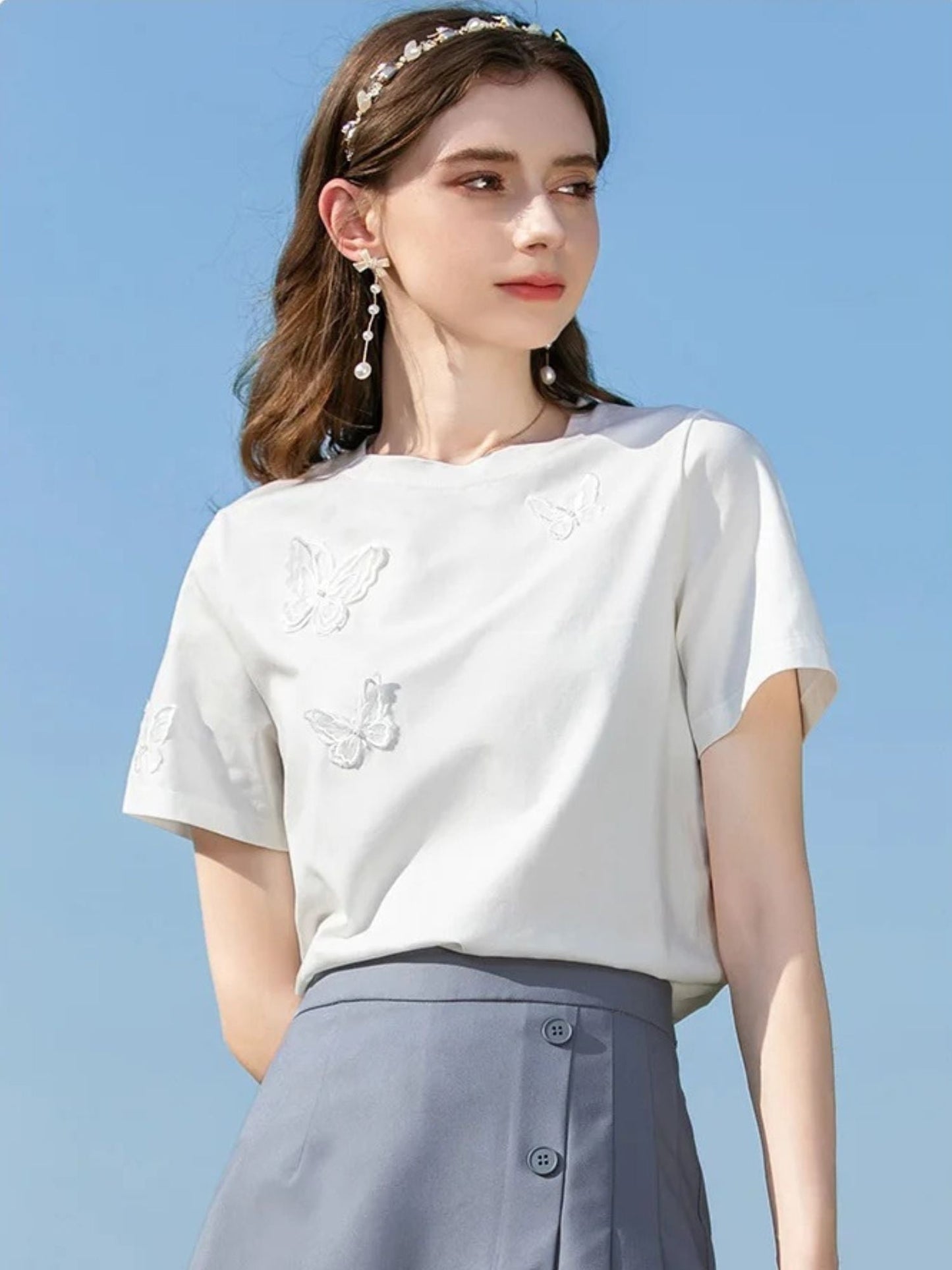 Woman in white embroidered shirt and skirt, smiling with hands behind her back.